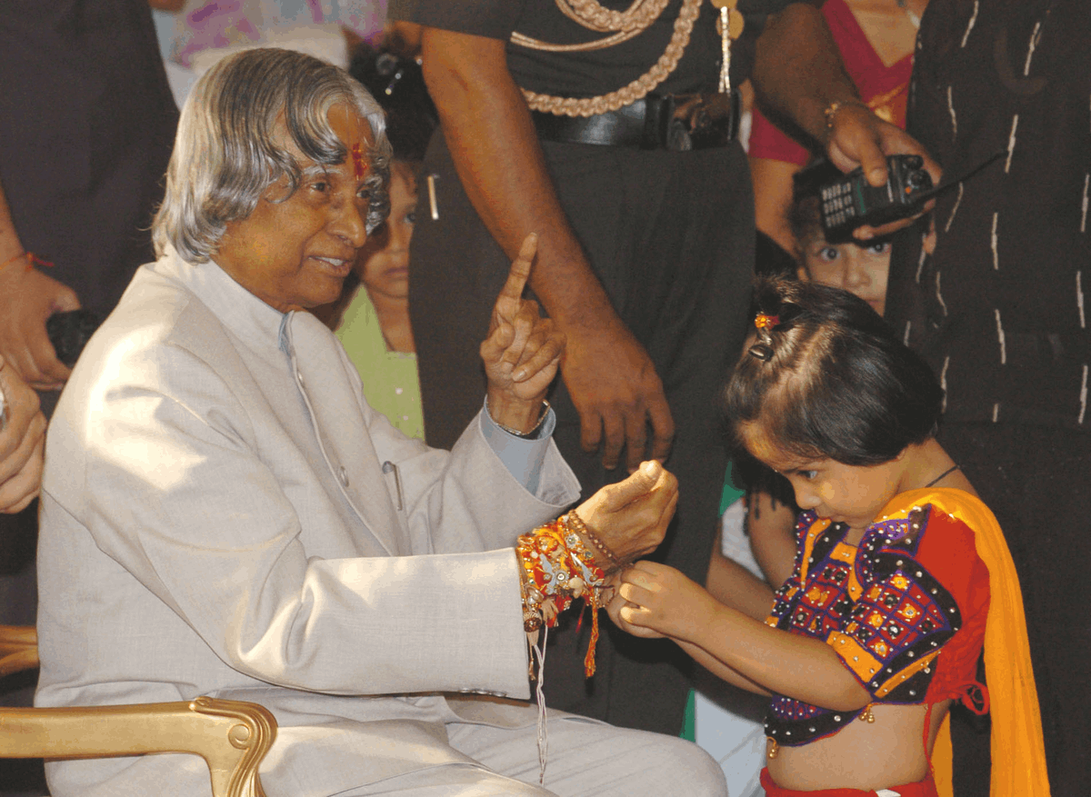 menina-amarrando-rakhi-presidente-apj-abdul-kalam-2005 Uma menina amarra um rakhi no pulso do presidente da Índia, Dr. A. P. J. Abdul Kalam, durante a celebração do Raksha Bandhan em Nova Délhi, em 2005.