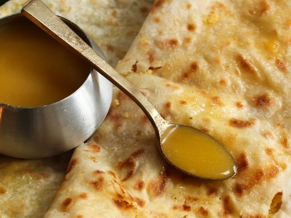 Aplicando ghee puro sobre Puran Poli quente, tradição que simboliza hospitalidade e sabor autêntico indiano