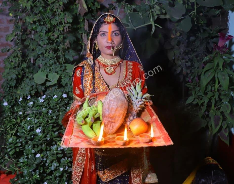 Devota em traje tradicional bihari segura um thali com oferendas enquanto realiza o sagrado ritual do Chhath Pooja