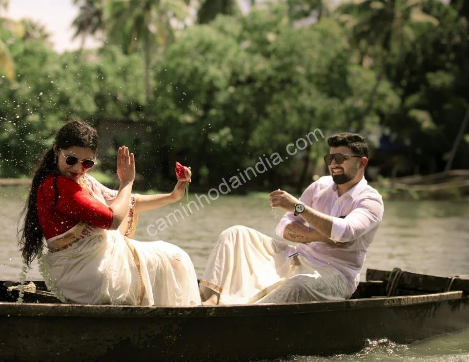 Um casal vestindo trajes tradicionais de Kerala — kasavu mundu e kasavu saree — navega serenamente pelos remansos, símbolo da beleza e cultura do estado